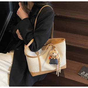 Model posing with white textured tote bag featuring brown leather trim and bear pendant