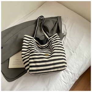 Détail du sac cabas en toile à rayures noires et blanches avec plaque logo dorée