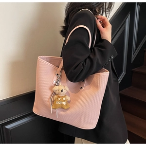 Détail d'un sac cabas rose gaufré à rayures diagonales avec charm ours porté par un mannequin
