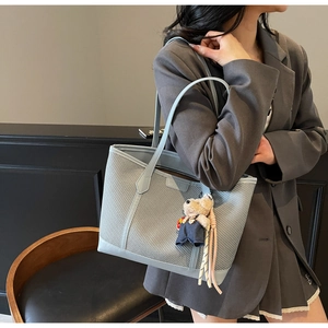 Detail of light blue woven tote bag with teddy bear pendant on a minimalist outfit