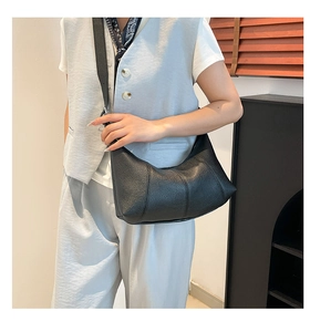 Detail of minimalist black pebbled leather baguette bag worn by a model
