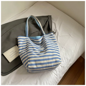 Détail du sac cabas en toile rayé bleu et blanc avec écusson ovale sur un lit blanc doux