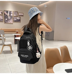 Detail of black backpack with Happy Mind print and plush bear charm in a cafe setting