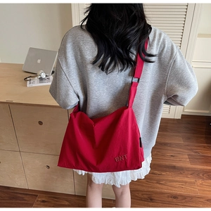 Detail of red canvas tote bag featuring BNT embroidery and adjustable strap for commuting