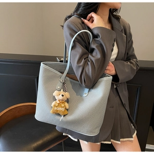 Détail d'un sac cabas tissé bleu clair avec un porte-clé ours en peluche sur un mannequin