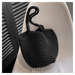 Close-up of black handmade crochet tote bag with textured rope weave on a minimalist chair