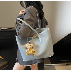 Détail d'un sac cabas bleu clair avec texture tissée et petit pendentif ours en peluche