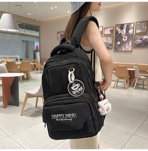 Close-up of black fabric backpack with white slogan and cute white plush bear pendant