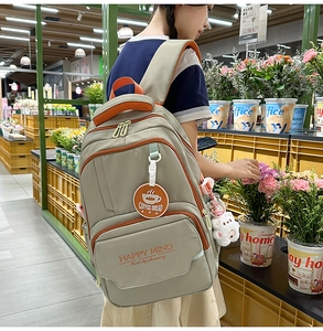Detail of khaki campus backpack with orange trim, featuring slogans and bear keychain