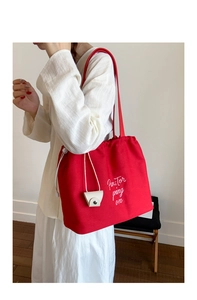 Detail of red canvas tote bag featuring drawstring closure and side leather pouch attachment