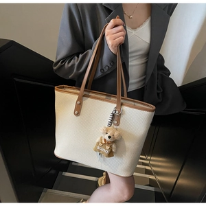 Détail d'un sac cabas tissé beige avec des anses en cuir marron et un pendentif ours en peluche