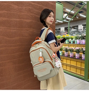 Detail of grey student backpack featuring orange straps and a cute plush doll charm