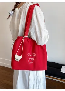 Detail of red canvas tote bag with drawstring closure and white letter embroidery