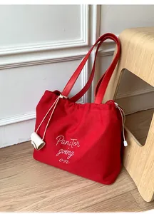 Detail of red canvas tote bag featuring white embroidery and drawstring closure