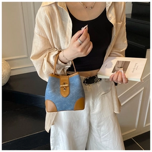 Close-up of blue denim bucket bag with brown leather trim and gold twist lock