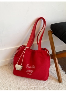 Detail of red canvas tote bag featuring white embroidery and drawstring closure