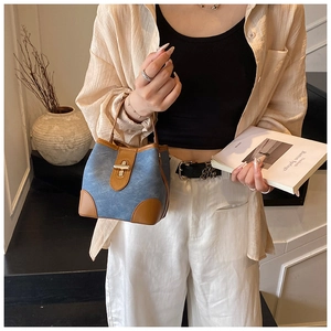 Close-up of a blue denim bucket bag with brown leather trim and gold metal buckle