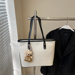 Détail du sac fourre-tout blanc tressé avec bordure en cuir noir et breloque ours