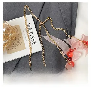 Detail view of golden chain with red beads and pink organza bow on grey fabric