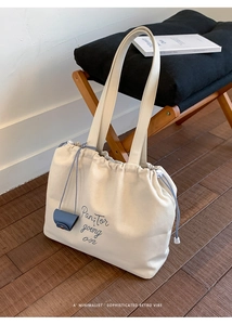 Detail of cream canvas tote bag featuring blue drawstring closure and chic embroidery