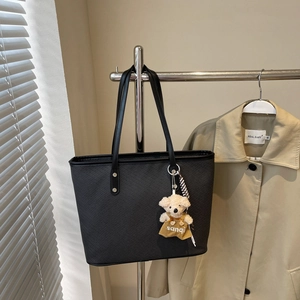Détail d'un cabas noir tressé avec pendentif ours sur un support d'exposition