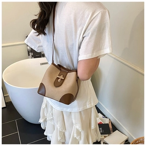 Model wearing a chic beige canvas bucket bag with brown leather trim and metal clasp