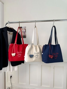 Detail of canvas drawstring tote bags in red, beige and navy with embroidered text