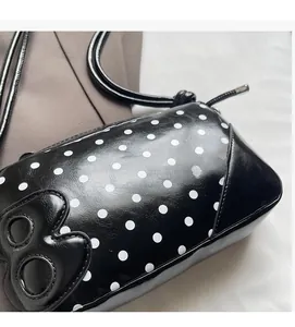 Detail of glossy black polka dot shoulder bag featuring a 3D letter B patch and zipper