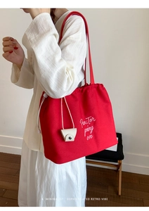 Detail of red canvas tote bag with drawstring closure and white embroidery on a model