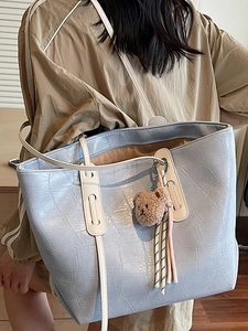 Hellblaue Shopper-Tasche mit Kroko-Prägung, weißen Trägern und Bärenanhänger am Modell
