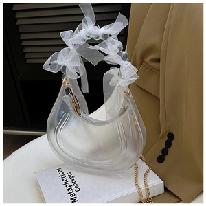 Close-up of clear crescent PVC bag with white lace bow handle and gold metal chain strap