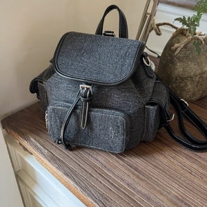 Detail of dark gray denim backpack with black leather trim on a vintage wooden bench