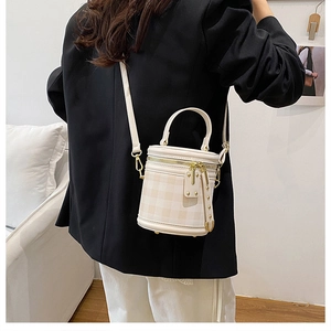 Close-up of quilted cylinder bucket bag in beige with gold zippers and leather strap