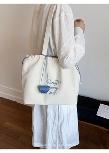 Detail of canvas tote bag with blue drawstring closure and embroidered front design