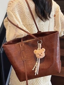 Braune Shopper-Tasche mit Krokodilprägung und Bärenanhänger an weiblichem Model