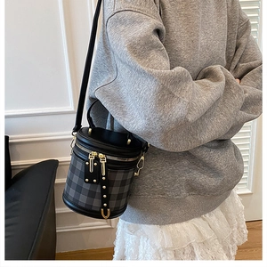 Close-up of a grey quilted cylinder bag with leather trim on a model in a grey hoodie