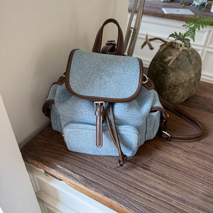 Detail of retro denim canvas backpack featuring brown leather straps and silver metal buckles