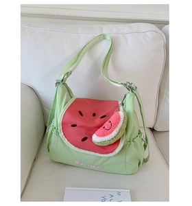 Detail view of watermelon crossbody bag showing embroidery and cute plush charm on a sofa