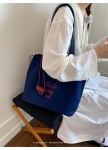 Detail of navy blue canvas tote bag featuring red embroidery and drawstring closure
