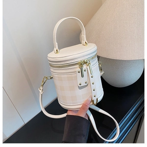 Detail view of white cylindrical bucket bag with quilted pattern and gold zip closure
