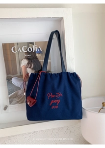 Detail of navy blue canvas drawstring tote with red embroidery and slim leather straps