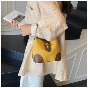 Detail view of yellow bucket bag with brown leather trim and golden twist lock closure