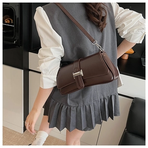 Detail view of a dark coffee leather baguette bag with silver buckle worn by a model