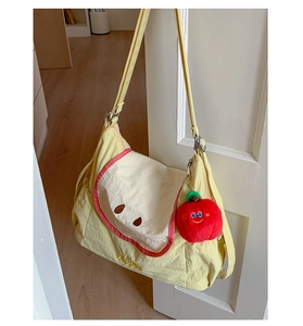 Detail of yellow apple-themed tote bag with red plush charm and adjustable strap