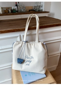 Detail of cream canvas tote bag with drawstring closure and blue lettering on wood stool