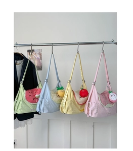 Detail showing four colorful fruit-themed nylon shoulder bags with plush charms hanging on a rack