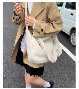 Street style view of cream canvas tote bag worn with a khaki trench coat for daily use