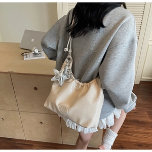 Detail of cream white pleated shoulder bag with silver star charm and knotted strap