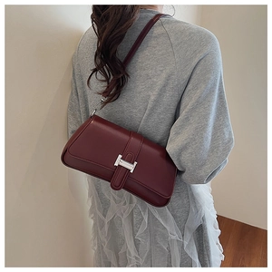 Detail view of the deep red leather shoulder bag featuring a silver metal H buckle on a model