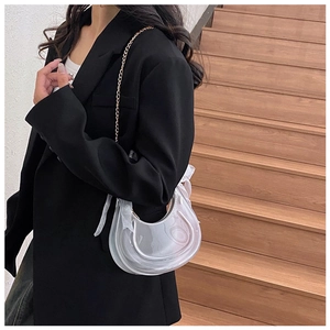 Detail of transparent crescent bag with white bow and gold chain on model